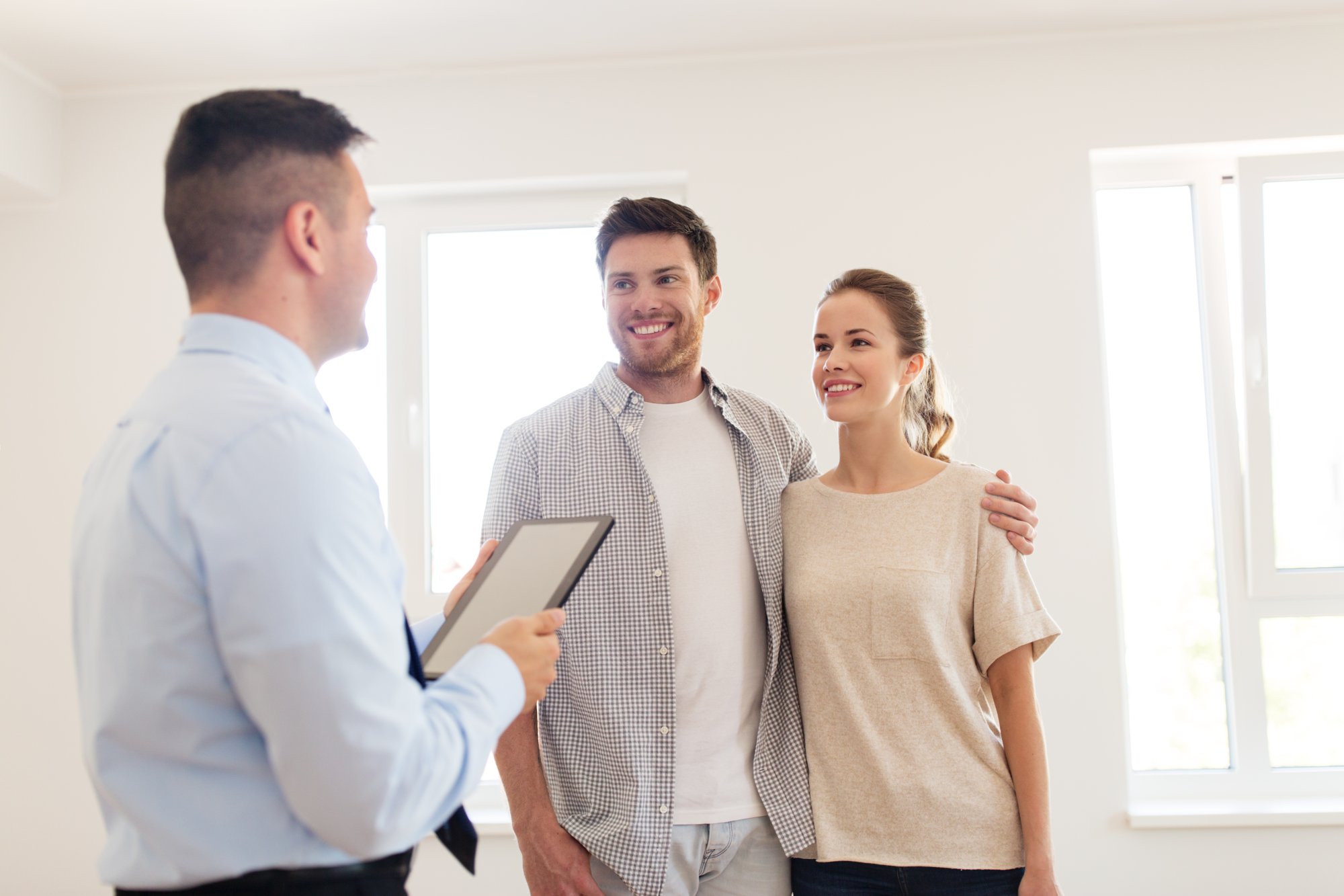 A couple viewing a bright apartment with a real estate professional using a tablet